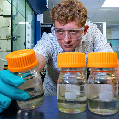 A scientist looks at three bottles of clear fuel in the lab.