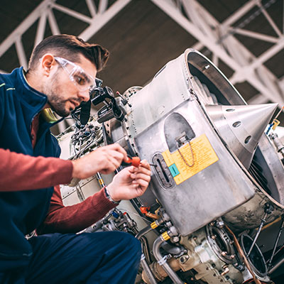 A mechanic repairs a jet engine in a hangar.